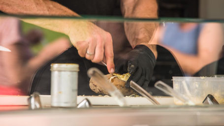 Zwei Hände bei der Zubereitung einer Kumpir - Detailaufnahme von Außen in den Food Truck