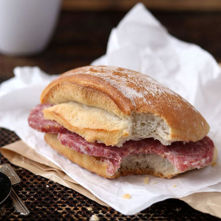 Ein angebissenes Küster-Brötchen mit dicken Stracke-Scheiben liegt auf Backpapier