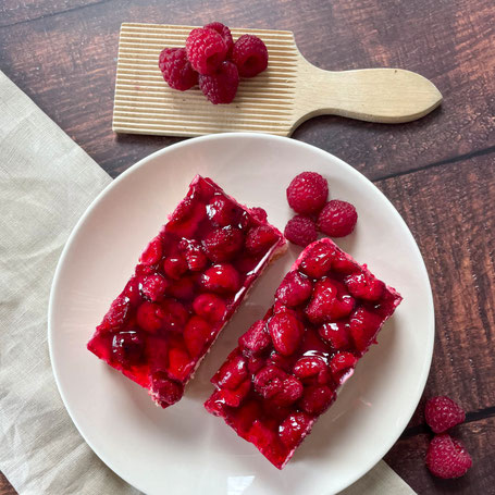 Zwei Stück Himbeer-Creme-Kuchen auf einem Teller, daneben mehrere frische Himbeeren