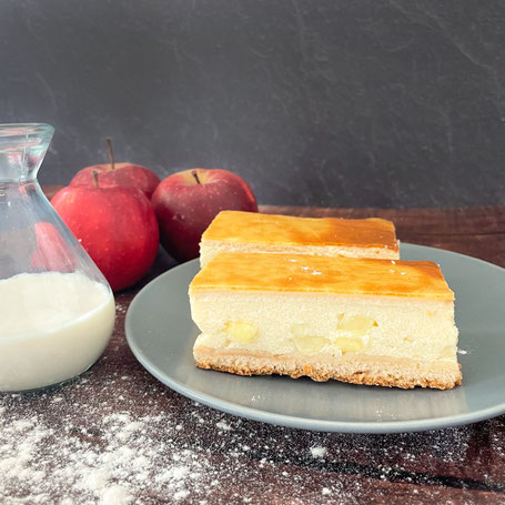 Zwei Stücke Apfel-Schmand-Kuchen auf einem Teller, mit Äpfel und einer Glaskaraffe daneben