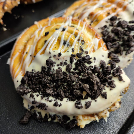 Plunderschnecke mit weißer Schokolade und zerbröselten Oreo-Keksen als Topping auf einem schwarzen Blech