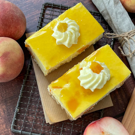 Zwei Stücke Maracuja-Pfirsch-Kuchen mit Glasur und Sahnetupfen, umgeben von frischen Pfirsichen auf einem Gitterrost