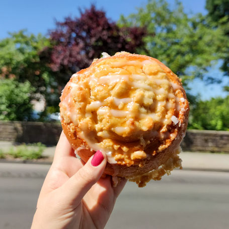 Ein Hefteil mit Streusel in der Hand, im Hintergrund Natur