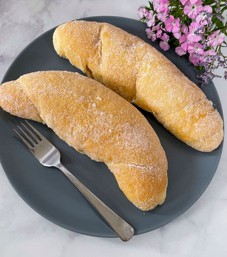 Zwei Vanillezapfen mit Zucker bestreut auf einem grauen Teller neben einer Gabel und rosa Blumen
