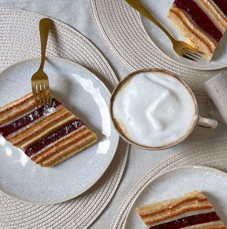 Mehrere mit Himbeer-Johannisbeer-Konfitüre durchzogenen Gebäcstücke auf Tellern, in der MItte steht eine Kaffeetasse