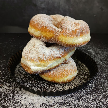 Drei aufeinander gestapelte Krapfen auf einem dunklen, runden Blech