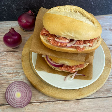 Zwei Schrippen mit Zwiebelmett auf einem Holzbrett, daneben rote Zwiebeln