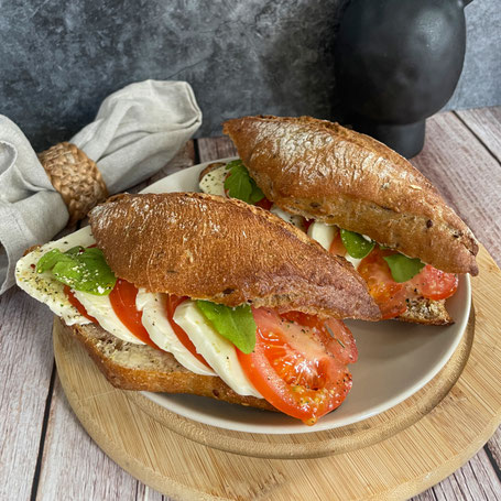 Zwei mit Tomate, Mozzarella und Rucola belegte Korny-Brötchen auf einem Teller