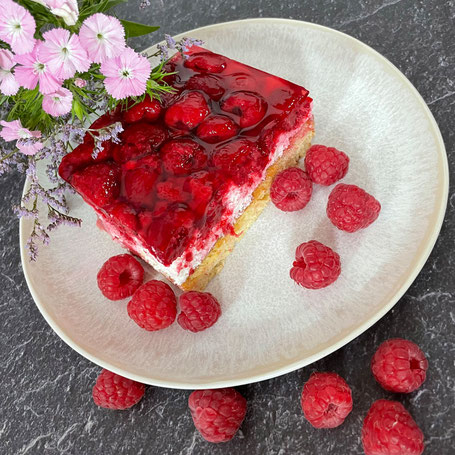 Ein Stück Himbeerkuchen auf einem Teller, umgeben von frischen Himbeeren