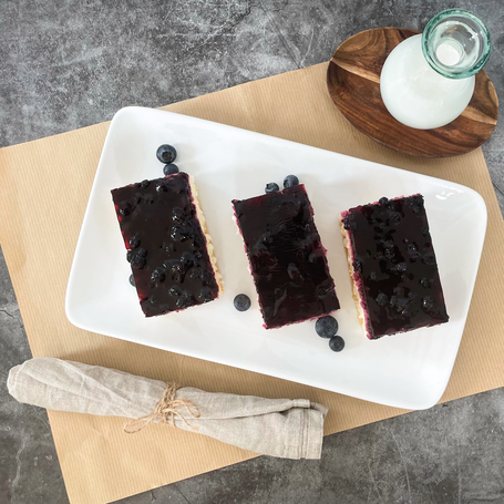 Drei Stück Heidelbeerkuchen auf einer weißen Platte mit ein paar frischen Heidelbeeren