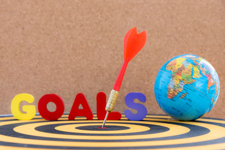 A dart perfectly hitting the target with the word "GOALS" and a globe, symbolizing clear objectives in Spanish learning.