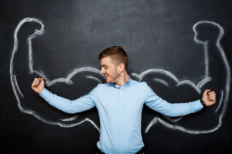 A smiling man flexing in front of a chalkboard with drawn muscles, representing confidence and motivation in learning Spanish.