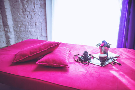 relaxing set on a bed in red satin sheets and pillows with camera and tea for relaxation