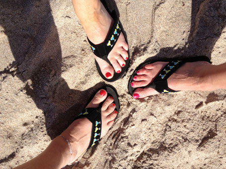 ladies showing their right foot on the beach with flip flops and fresh pedicure in red colour