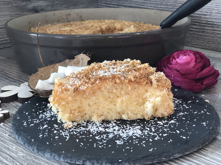Springform in rund aus Ton in der Farbe grau mit Kuchenteig gefüllt. Kuchenstück auf Schieferplatte angerichtet
