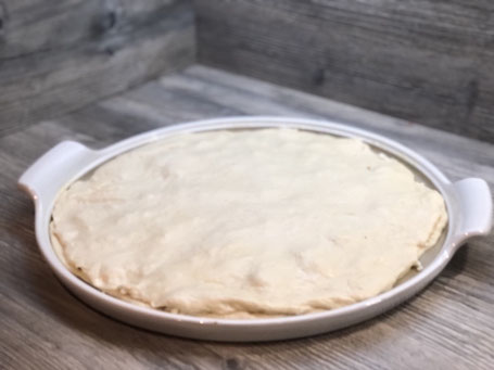Runde weißer Stoneware-Form auf Arbeitspalatte mit Fett bestrichen und Pizzateig belegt