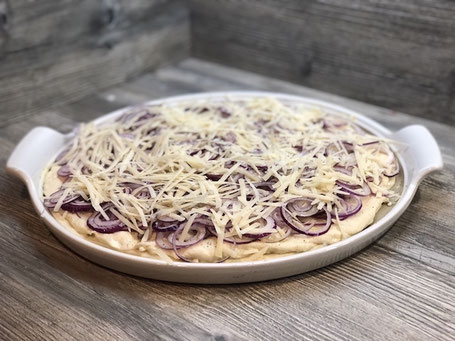 Runde weißer Stoneware-Form auf Arbeitspalatte mit Fett bestrichen, Pizzateig belegt und Zwiebeln und Käse belegt