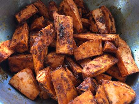 Süßkartoffelspalten mit der Gewürzmischung vermischt in einer Metallschüssel