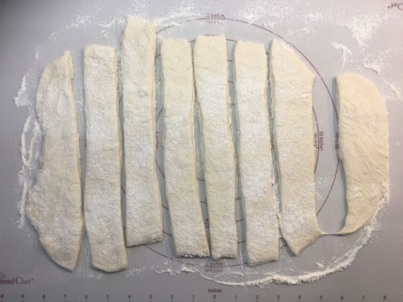 Brötchenteig auf einer Backmatte ausgerollt und in Streifen geschnitten