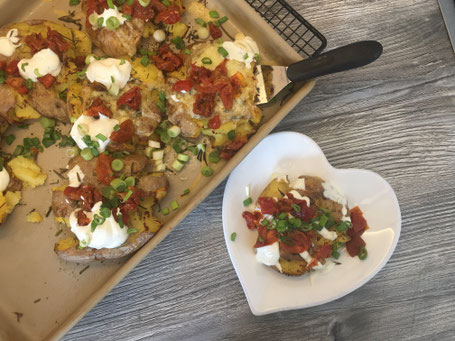 Fertig angerichtete Quetsch-Kartoffeln mit Käse, Tomaten, Frühlingszwiebeln und Aioli garniert
