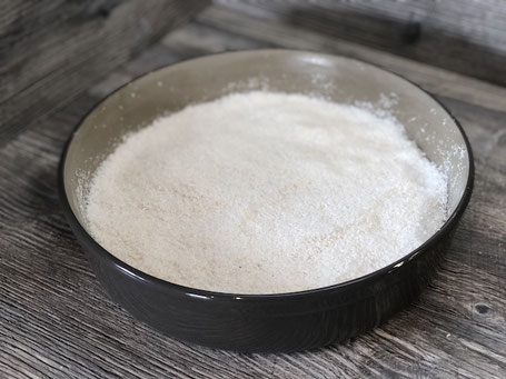 Springform in rund aus Ton in der Farbe grau mit Kuchenteig gefüllt und Kokosflocken bestreut