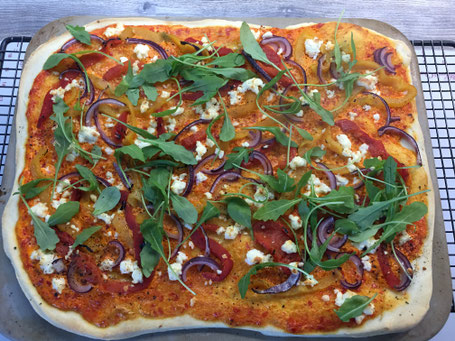 Fertig gebackene Pizza mit Gemüse und Rucola vom Tonbackstein