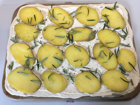 Zauberstein mit ausgerolltem Pizzateig und Schmand bestrichen, Kartoffeln und Rosmarinnadeln belegt
