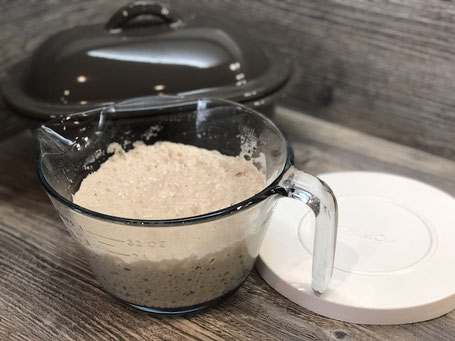 Glasschüssel mit Brotteig und Brotbackform aus Ton in grau