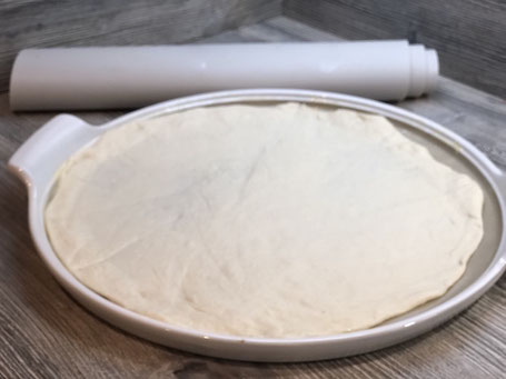 Runde weißer Stoneware-Form auf Arbeitspalatte mit Fett bestrichen und Pizzateig belegt