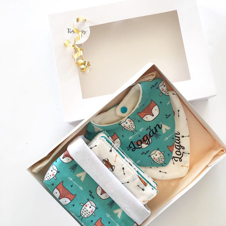 Cette image représente une box naissance composée de 2 bavoirs, d'un semainier de lingettes et sa panière assortie au motif de renards