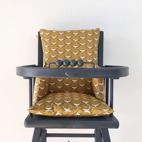 Cette image représente un coussin de chaise haute de couleur camel pour chaise haute en bois