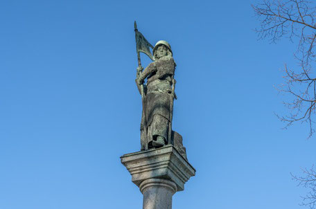 Bewaffnete Frauenskulptur mit Banner unter blauem Himmel