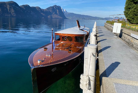 A wooden, shining boat lies on the pier. A wooden, shiny boat lies on the jetty. Lake Lucerne and green hills can be seen behind it.