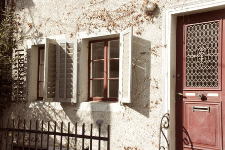 Two windows with red frames, open shutters and a red door to the right.