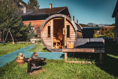 Das Saunafass mit dahinterliegendem Haupthaus, in welchem sich das Badezimmer befindet.
