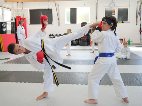 Karate Schüler führt eine Karate Technik aus am Partner. Fußkick zum Kopf, Partner block den Fußkick. Selbstbewusst und Stark. 