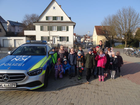 Die erste Klasse mit Polizistin Frau Zeiher neben dem Polizeiauto auf dem Schulhof