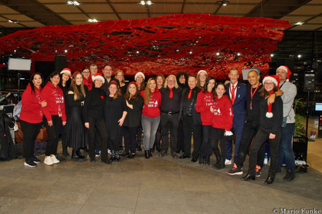 Gruppenfoto von UGC und beteiligtem Flughafen-Team vor der roten Deckenkunst des Terminal 1