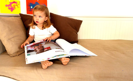 Kind auf Sofa liest ein Kleine Künstler Kinderkunstbuch mit den Bildern eines zweijährigen Kindes