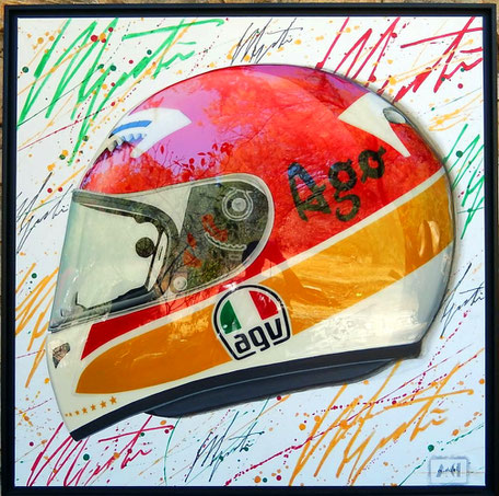 Sur un fond blanc recouvert de signatures "Agostini" en jaune, rouge, et vert le casque AGV du pilote, semblant en relief brille de mille feus