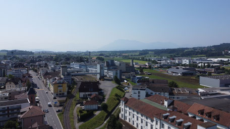 Blick von der Baldeggerstrasse über die Milchverarbeitung und die ehemalige Schokoladenfabrik im Vordergrund,  mit den Innerschweizer Berge im Hintergrund.