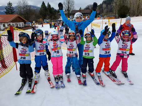 7 kinder mit startnummern u. erhobenen händen, skilehrerin