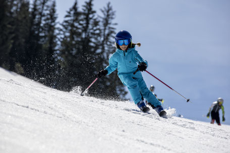 Mädchen in blauem skianzug bei der kurvenfahrt