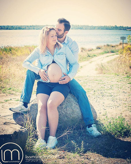 Babybauch Fotos, Schwangerschaftsshooting Schwangere mit dem Papa auf einem Stein sitzend