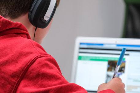 Un élève avec un casque d'écoute et devant un ordinateur suit un cours en ligne.