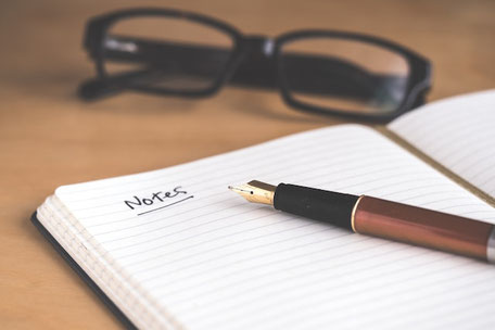 Des lunettes se trouvent à côté d’un cahier sur lequel est inscrit Notes. Un stylo-plume se trouve sur le cahier.