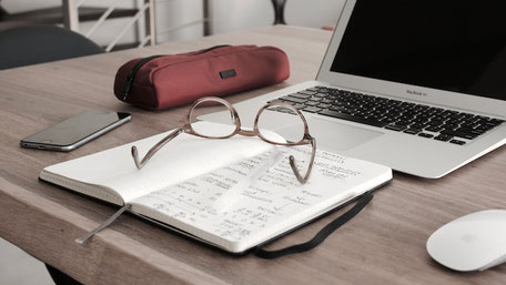 Un cahier, des lunettes, une trousse, un téléphone intelligent et un ordinateur sont sur une table.