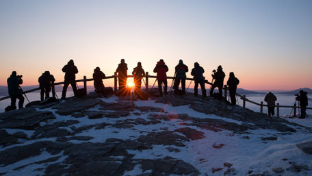 A group of photographers taking a picture of a sunrise from a mountain top 