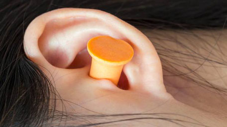 An asian woman using ear plugs to block out unwanted noises while she sleeps