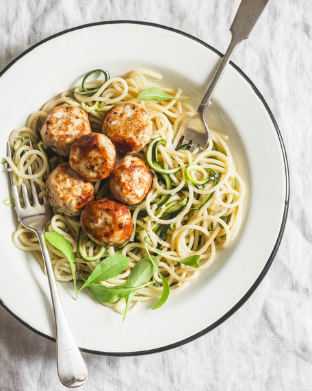 Spaghetti with cheesy chicken meatballs and zucchini noodles. Delicious lunch on a light background, top view